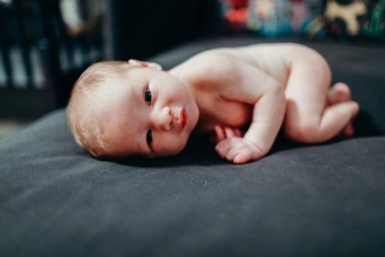 Say Hello To Rhonan 10 Adorable newborn baby lying on a dark bed, looking at the camera.