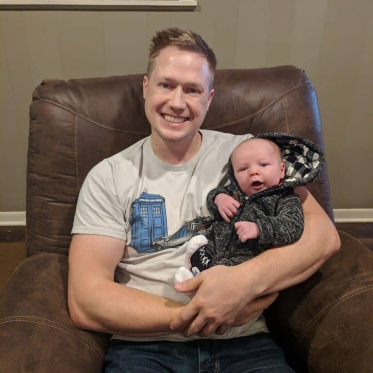 Say Hello To Rhonan 9 Smiling man holding a baby on a brown armchair.