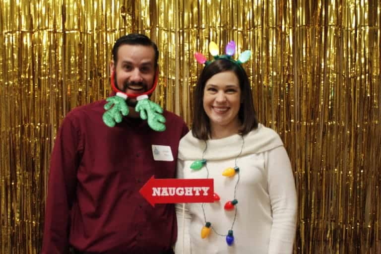 Two people at Christmas party with festive accessories and gold backdrop.