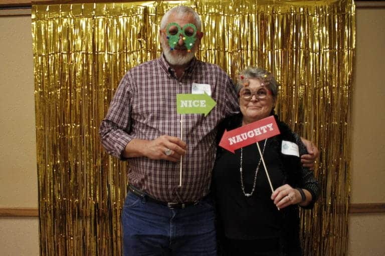 Man and woman in festive masks holding 'Nice' and 'Naughty' signs.
