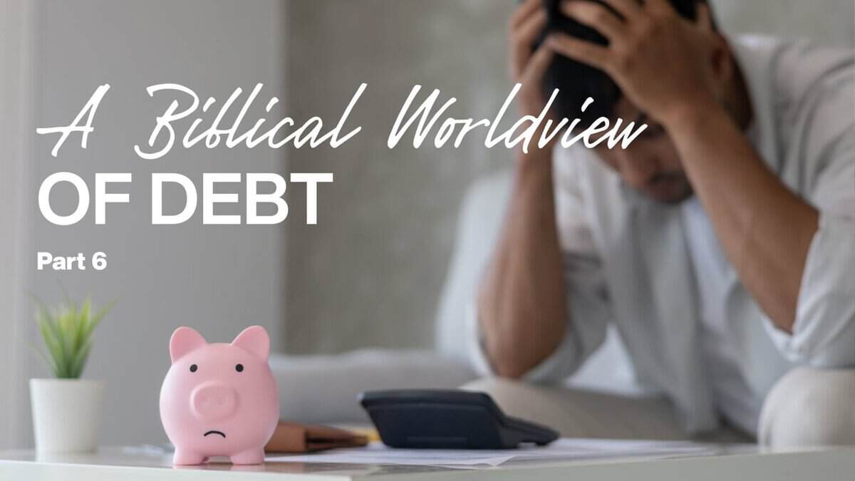 Man stressed about debt with head in hands and piggy bank on desk.
